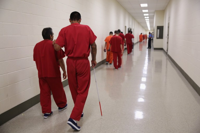 ADELANTO, CA - NOVEMBER 15: A blind detainee walks with a fellow immigrant at the Adelanto Detention Facility on November 15, 2013 in Adelanto, California. The facility, the largest and newest Immigration and Customs Enforcement (ICE), detention center in California, houses an average of 1,100 immigrants in custody pending a decision in their immigration cases or awaiting deportation. The average stay for a detainee is 29 days. The facility is managed by the private GEO Group. ICE detains an average of 33,000 undocumented immigrants in more than 400 facilities nationwide. (Photo by John Moore/Getty Images)