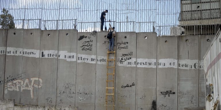Palestinian men climb the separation wall at the town of al-Ram to illegally cross into Jerusalem, Sunday, Sept. 15, 2024. (AP Photo/Mahmoud Illean)