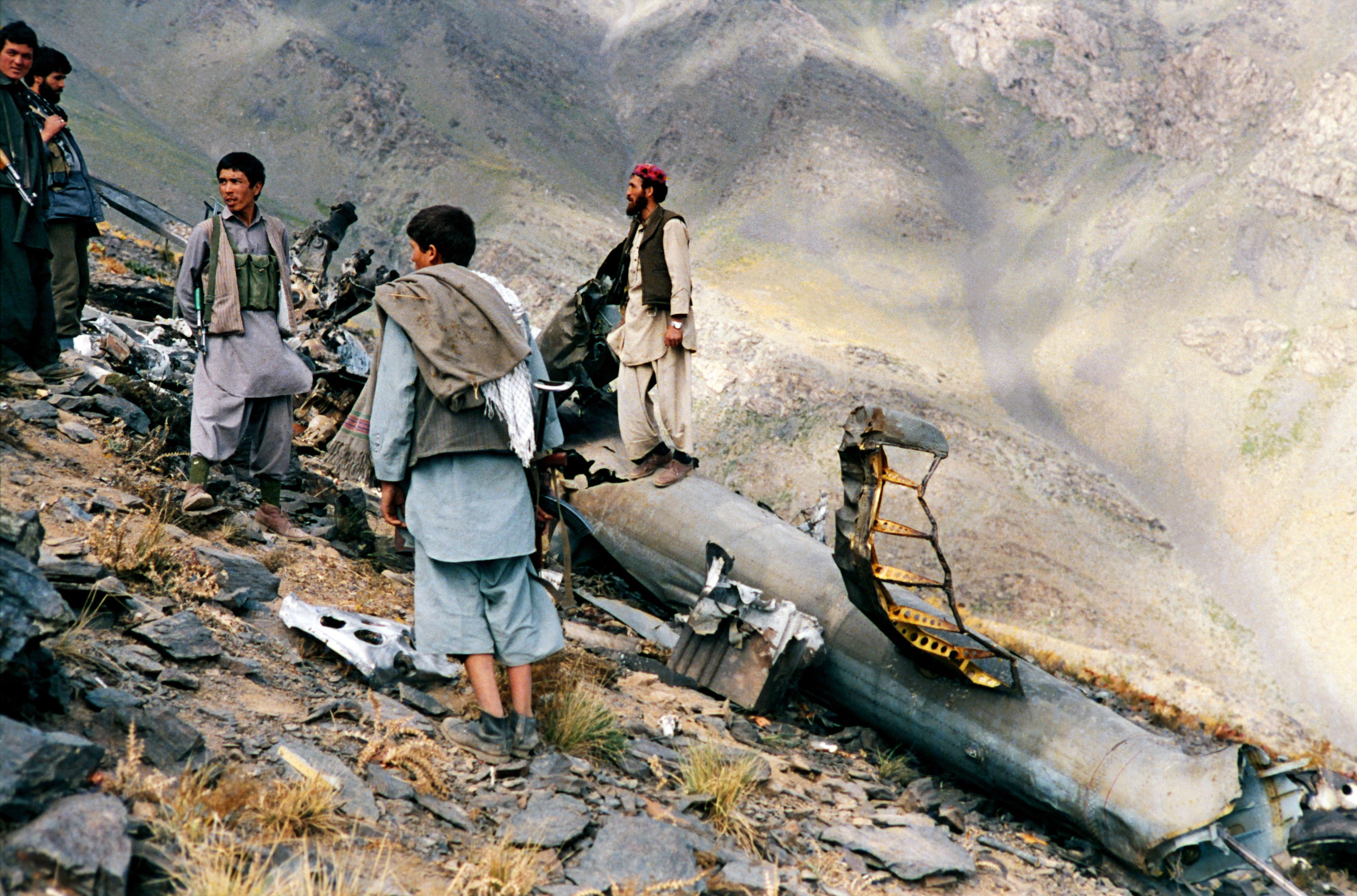 TOPSHOT - Mujahidin (mujahideen) of the Harakat-e Islami Party of Afghanistan stand beside the debris of an helicopter they had shot down with a stinger missile in sanglakh valley, Maiden Province (west of kabul) in afghanistan at the end of June. (Photo by AFP) (Photo by -/AFP via Getty Images)