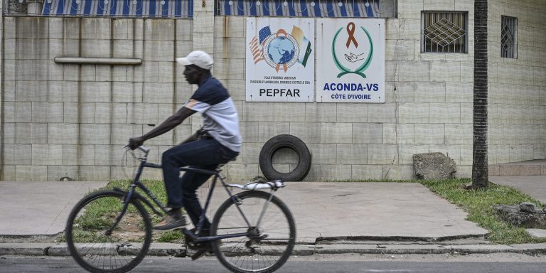 A cyclist rides past a PEPFAR sign in Abidjan on July 12, 2025. (Photo by Issouf SANOGO / AFP)