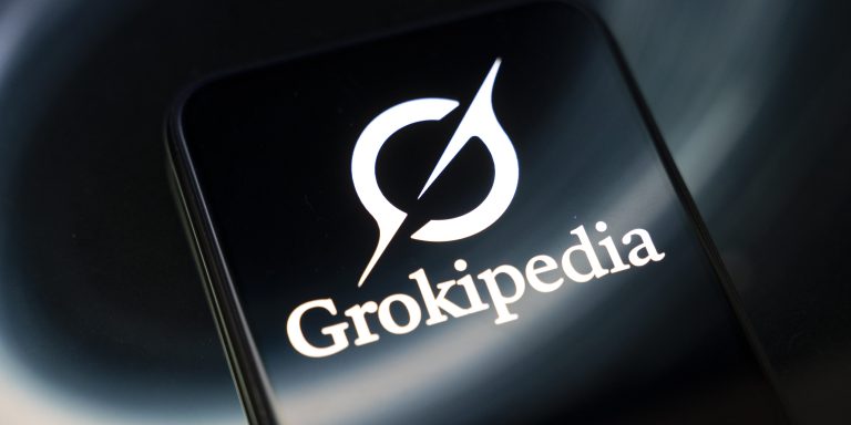 The Grokipedia encyclopedia logo appears on a smartphone screen reflecting an abstract illustration. The encyclopedia is entirely generated by Grok AI and is intended to be an alternative to Wikipedia, according to Elon Musk, in Creteil, France, on October 29, 2025. (Photo by Samuel Boivin/NurPhoto via Getty Images)