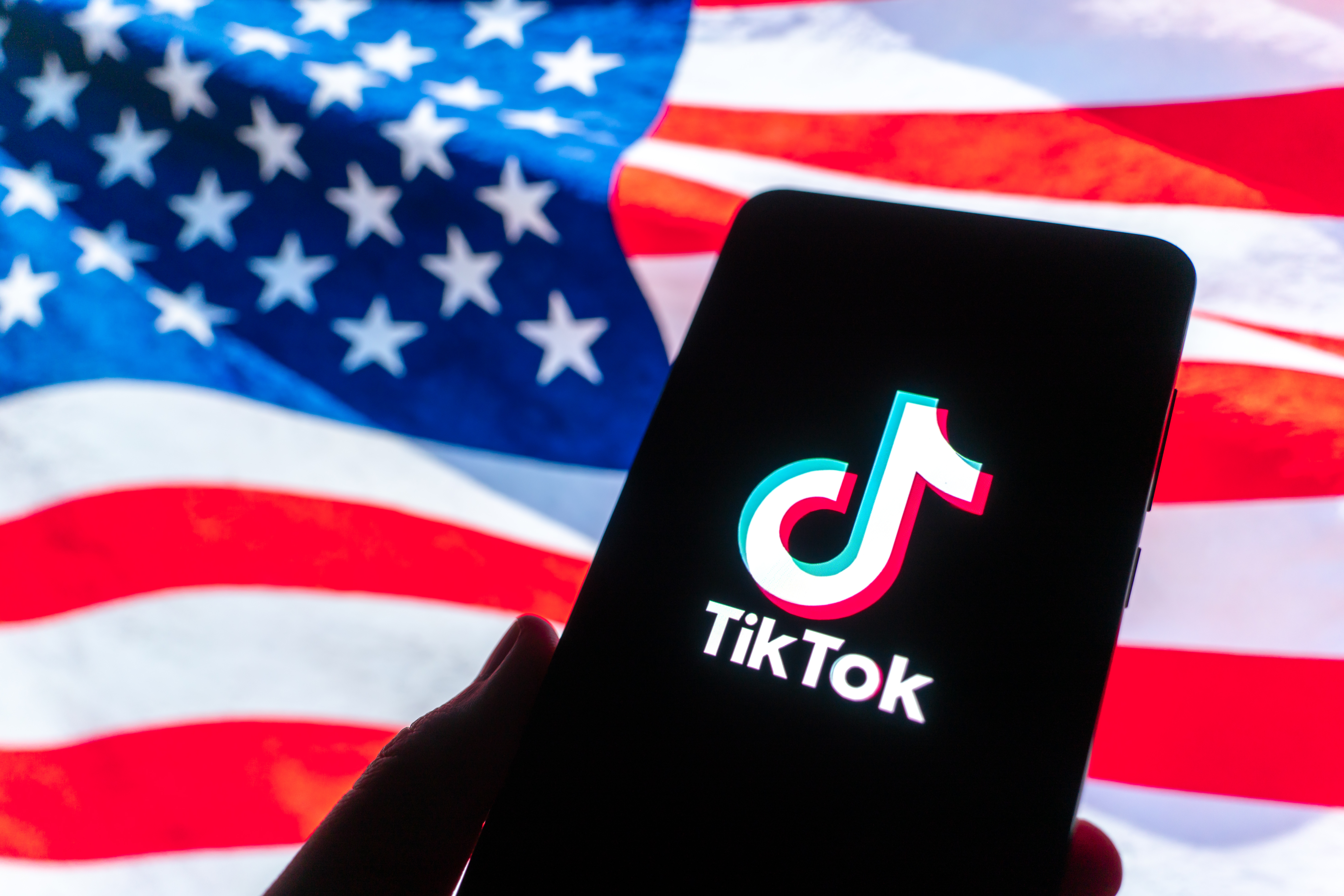 GUANGZHOU, CHINA - DECEMBER 19: In this photo illustration, the logo of TikTok is displayed on a smartphone screen with a US national flag in the background on December 19, 2025 in Guangzhou, Guangdong Province of China. TikTok's Chinese owner ByteDance has signed binding agreements with US and global investors to operate its business in America, TikTok's boss told employees on December 18. (Photo by Qin Zihang/VCG via Getty Images)